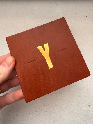 Tan square leather coaster with gold foil detail made for the Y code.